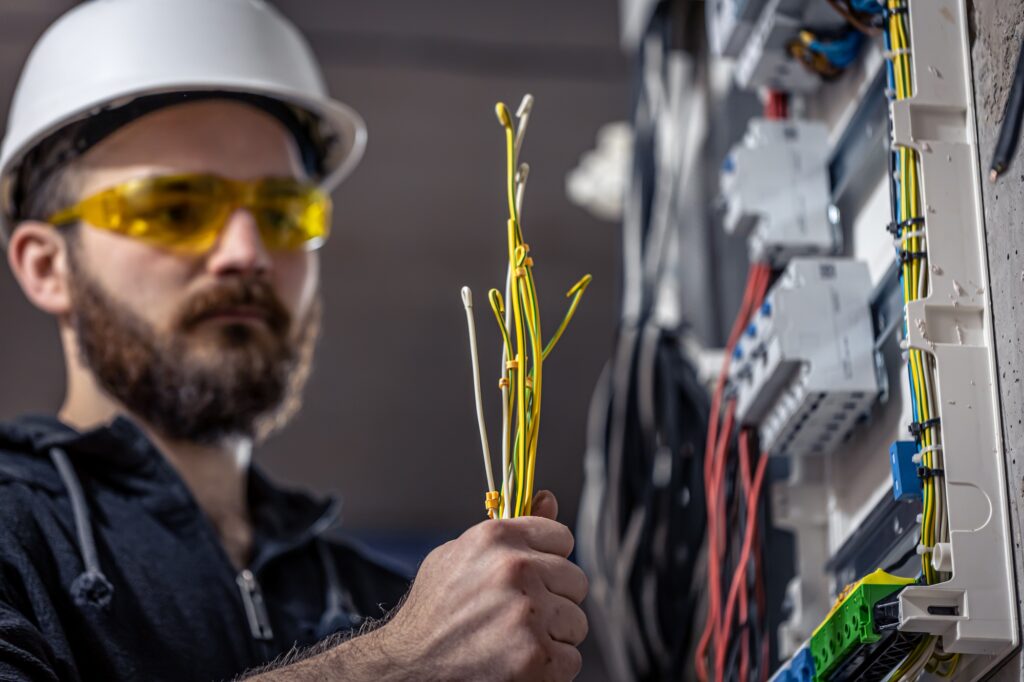A male electrician works in a switchboard with an electrical connecting cable.